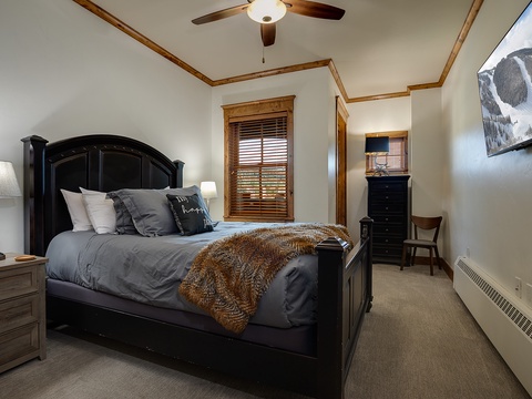 Unwind in your private bedroom with a plush bed draped in cozy throws, soft bedside lighting, and a ceiling fan overhead. Your mountain retreat awaits with warm wood accents and inviting comfort.