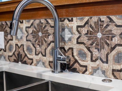 A sleek modern faucet complements artisan wood-look tile with geometric patterns, blending contemporary functionality with warm rustic character in your well-appointed kitchen.