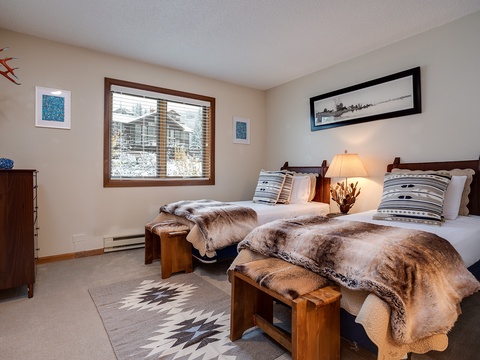 Cozy twin beds with plush faux-fur throws invite restful sleep, while rustic wood furnishings and mountain-inspired artwork create a warm, welcoming retreat after your day of adventure.