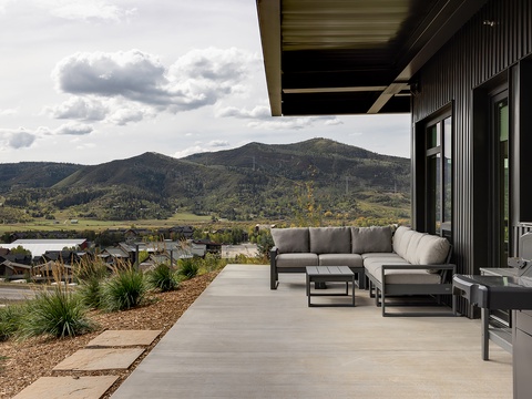 This covered terrace offers dramatic mountain and lake vistas with comfortable lounge seating and an outdoor grill, perfect for relaxing or entertaining while surrounded by stunning natural scenery.