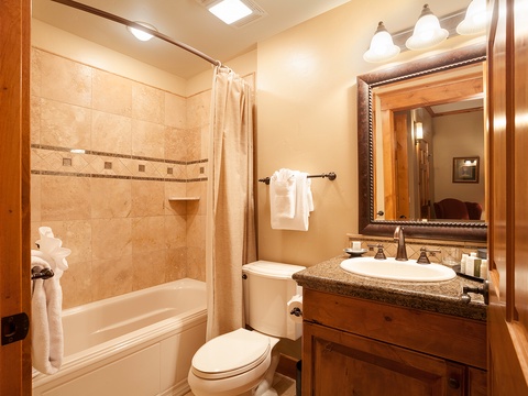 Your private bathroom features a spacious tub, elegant tile detailing, plush towels, and warm wood accents that create a cozy mountain retreat feel.