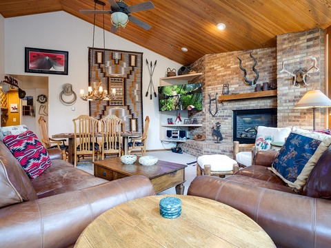 Sink into plush leather sofas in a striking vaulted living room where rustic charm meets modern comfort. Rich wood ceilings, exposed brick, and a glowing fireplace create your perfect retreat.