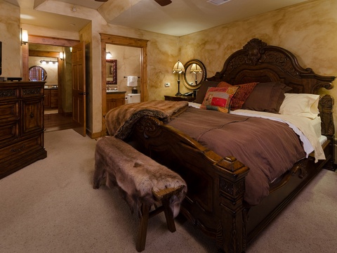 Sink into the plush bedding and ornate carved headboard of your luxurious retreat, where warm lighting and rich textures create an inviting atmosphere for restful nights.