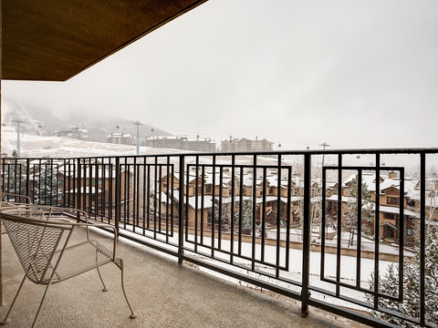 A winter balcony overlooking a snow-covered alpine village with ski lifts ascending toward misty mountain slopes.