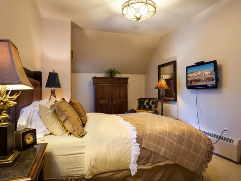 Sink into plush bedding beneath warm lighting and rustic elegance. Your charming retreat features antique touches, a cozy reading chair, and mountain views on screen—perfect for unwinding after adventure.