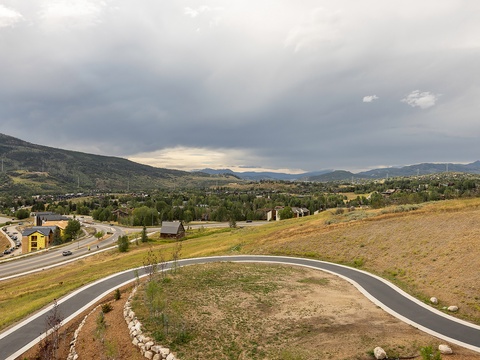 An elevated perspective of the surrounding neighborhood reveals rolling hills, residential areas, and mountain ranges under a dramatic cloudy sky, showcasing the property's picturesque location.