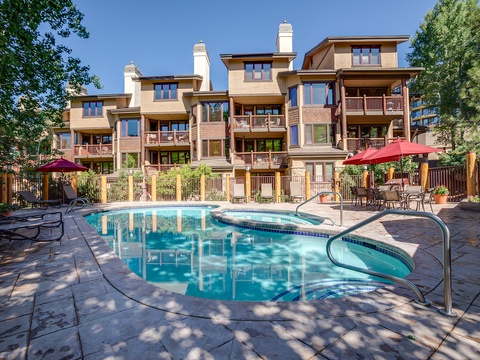 Multi-level property complex with swimming pool, patio seating, and scenic mountain backdrop—nestled in a tree-lined setting near popular area attractions.