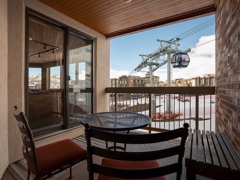 A ski resort gondola glides past this balcony, providing convenient mountain access. The covered outdoor space features seating with views of the slopes and surrounding village buildings.