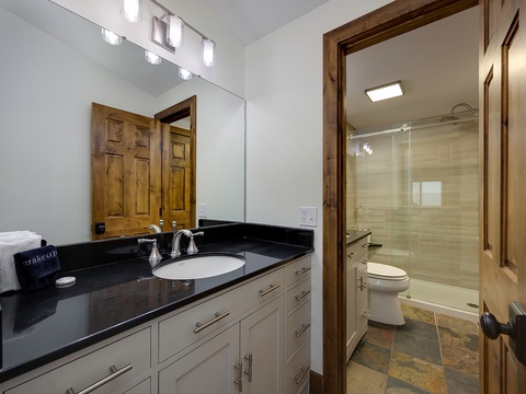 Your private retreat features a spacious vanity with sleek black countertops and a spa-like en-suite with a glass-enclosed shower, offering modern comfort and style.