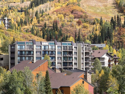 Modern multi-level buildings situated in a forested mountain valley, surrounded by evergreen and golden aspen trees during autumn season.