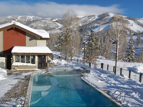 An outdoor heated pool overlooking pristine ski slopes and snowy mountain peaks, perfect for unwinding after a day on the slopes.