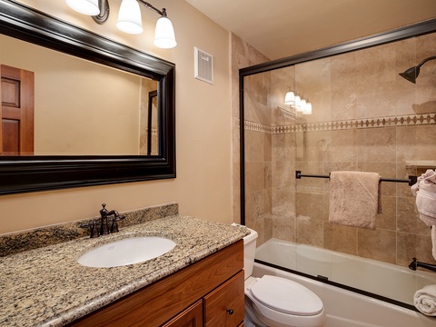Step into your private bathroom featuring a granite vanity, spacious tub with shower, and soft towels ready for your arrival. The warm tones and thoughtful details create a soothing retreat.