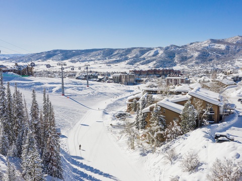 Panoramic view of a snow-covered ski resort village nestled in pristine mountain terrain, featuring slopes, gondola lifts, and accommodations set against a clear winter sky.