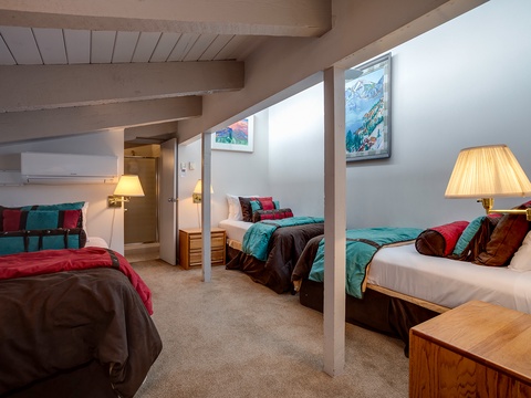 Three comfortable beds await in this spacious room, perfect for gathering your group after a day of adventure. Warm lighting and vibrant mountain artwork create a cozy alpine retreat.