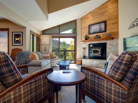 Sink into plush seating by your cozy stone fireplace, where vaulted ceilings and mountain views through expansive windows create your perfect retreat.