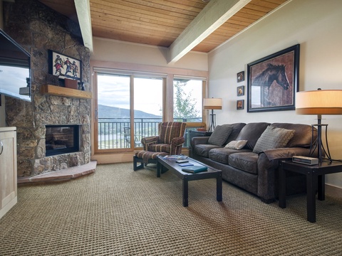 Sink into the plush sofa by the stone fireplace and enjoy stunning mountain views through expansive windows. The warm wood ceiling and cozy seating create your perfect retreat after a day exploring.