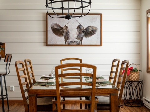 Gather around this charming farmhouse dining table, where rustic warmth meets countryside personality. Enjoy your meals beneath a whimsical cow portrait and stylish cage pendant light.