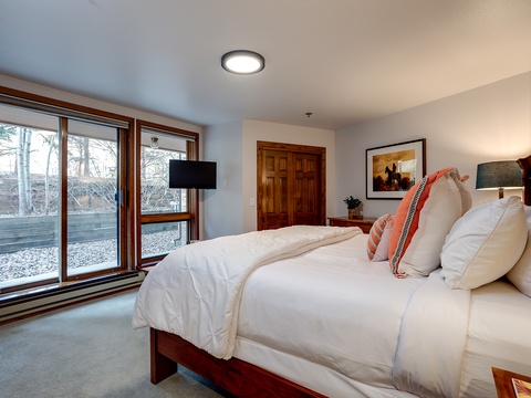 Sink into plush bedding in this serene bedroom where natural light streams through large windows, revealing tranquil outdoor views. Your peaceful mountain escape awaits.