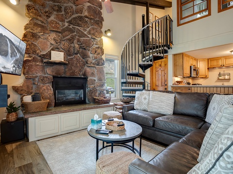 Relax in your open-plan living area with vaulted ceilings, charming stone fireplace, and cozy leather seating—where rustic elegance meets home comfort.