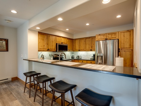 You'll love gathering around this spacious kitchen's breakfast bar, fully equipped with modern appliances and warm wood cabinetry, perfect for preparing meals and sharing morning coffee.