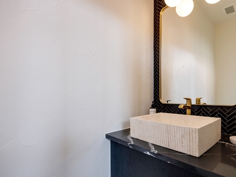 You'll appreciate the elegant bathroom featuring a designer vessel sink, gleaming brass fixtures, and a chic herringbone-tiled accent wall that frames the vanity mirror.