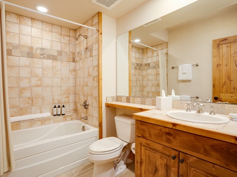 Step into your private bathroom with warm wood accents, a deep soaking tub with elegant tiled surround, and a spacious vanity—your personal retreat awaits.