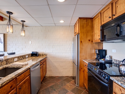 Your fully equipped kitchen features granite countertops, rich knotty pine cabinets, and modern appliances including a microwave, stove, and full-size refrigerator—perfect for preparing home-cooked meals during your stay.