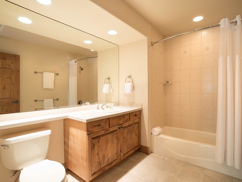 Step into your spa-like private bathroom featuring a soaking tub, warm lighting, and rustic wood vanity. Plush towels and ample space ensure your comfort and relaxation.