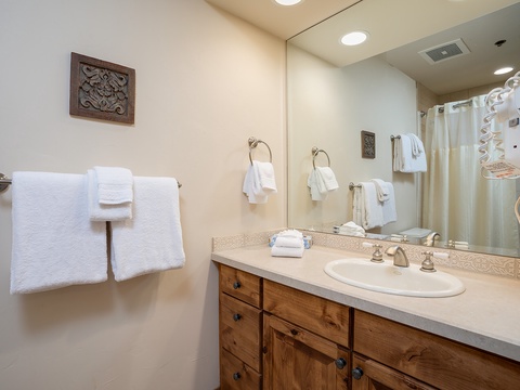 Your private bathroom features a spacious vanity with warm wood cabinetry, fresh towels, and a well-lit mirror—perfect for preparing each day of your stay.