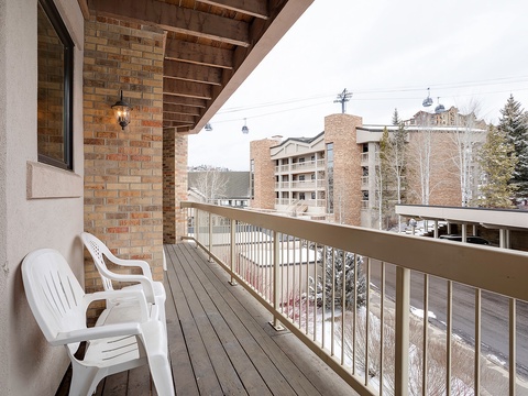 A balcony positioned in a ski resort area with views of nearby buildings, slopes, and ski lifts, situated within a mountain village setting.