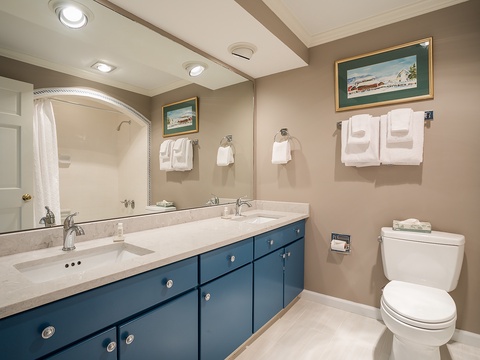Relax in your spacious private bathroom featuring dual sinks, generous counter space, soft linens, and coastal artwork that sets a serene tone for your stay.