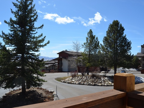 The property is nestled in a scenic mountain setting with mature evergreens, natural landscaping, and expansive blue skies, offering a serene retreat atmosphere.