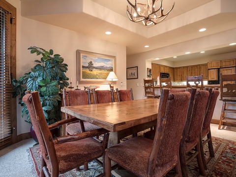 Gather around this spacious dining table where laughter flows freely over shared meals. The warm wood and antler chandelier create an inviting mountain retreat atmosphere for your memorable vacation dinners.