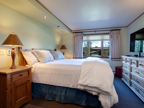 Your peaceful retreat awaits with a plush bed, warm wood furnishings, and mountain views framed by charming curtains. Unwind in this cozy space designed for your comfort.