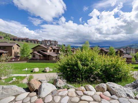 Scenic mountain resort area nestled among rolling hills with nearby residential and vacation properties. Lush spring landscaping frames the surrounding neighborhood beneath dramatic alpine skies.