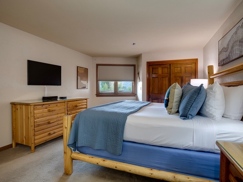 Unwind in your cozy bedroom with a plush bed, warm wood accents, and mountain views framed by the window—your peaceful mountain retreat awaits.