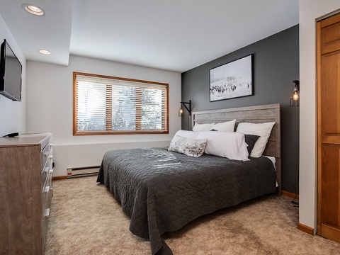 Sink into plush bedding and unwind in your modern bedroom, featuring cozy wood accents, mountain views through the window, and a smart TV for entertainment.