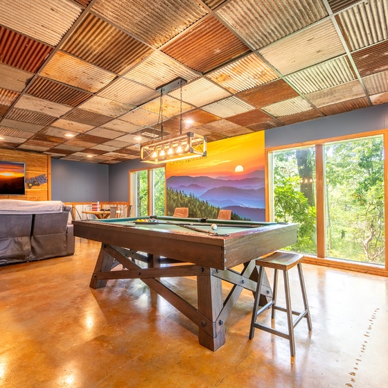 Your game room features a unique patchwork ceiling and natural light streaming through large windows. Challenge friends to pool under warm lighting, or relax on the cozy sofa—a perfect retreat for fun and connection.
