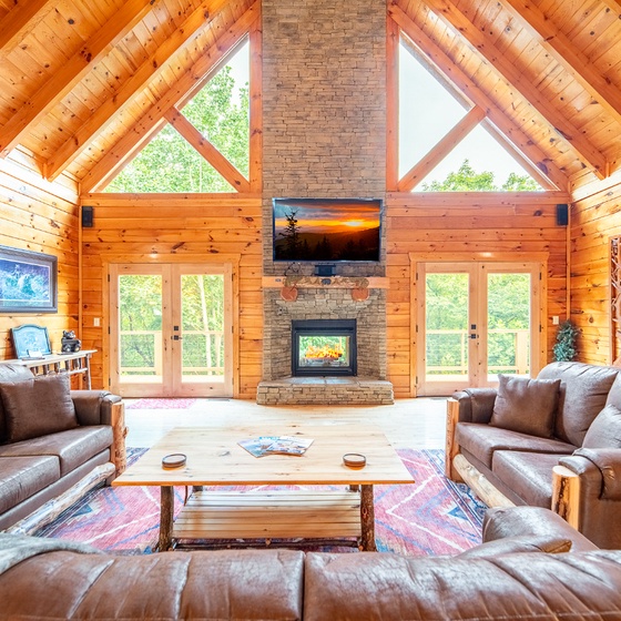 Gather with loved ones in this stunning great room, where vaulted wood-beam ceilings and a towering stone fireplace create a warm, inviting retreat. Natural light pours through floor-to-ceiling windows, framing peaceful forest views.
