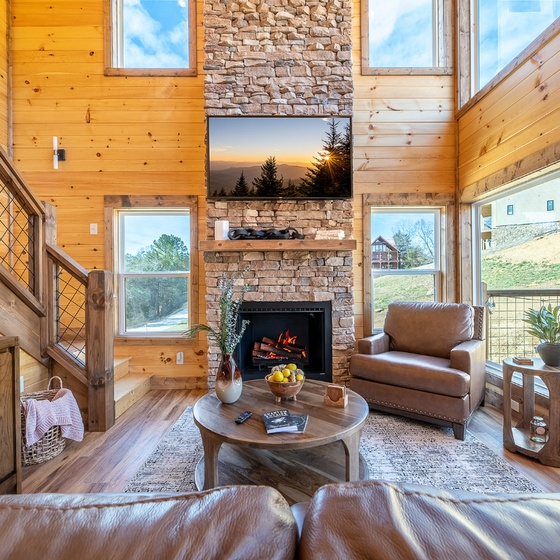 Unwind in your cozy living room by the stone fireplace, surrounded by warm wood and natural light streaming through expansive windows.