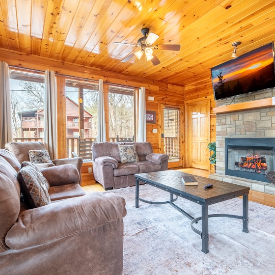 Cozy up in your rustic living room with plush leather seating, crackling fireplace, and mountain views through floor-to-ceiling windows.