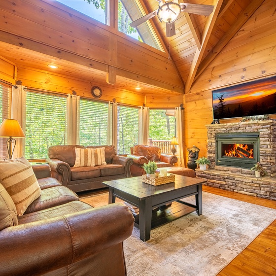 Sink into plush leather seating beside your crackling stone fireplace while cathedral ceilings and sunlight through tall windows create your perfect mountain retreat sanctuary.