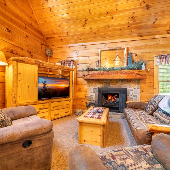 Curl up in your cozy cabin living room, where rustic walls surround plush seating and a crackling stone fireplace.