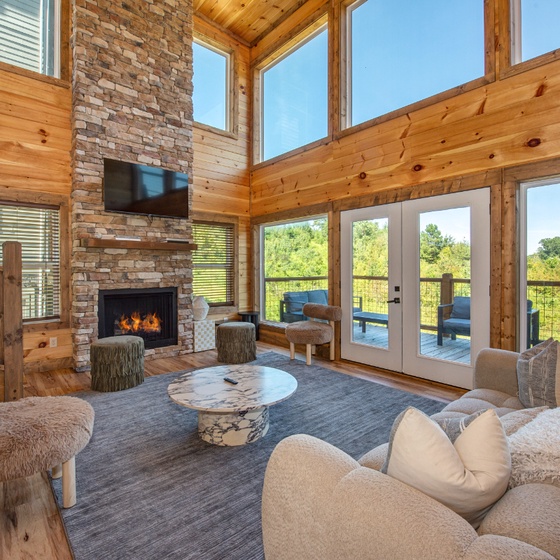 Sink into plush seating beside your crackling stone fireplace while soaking in natural light and views through floor-to-ceiling windows—a cozy retreat blending rustic charm with modern comfort.