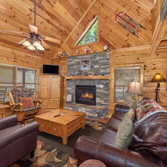 Cozy up by your stone fireplace in this rustic living room with vaulted ceilings and leather seating for mountain getaway relaxation.