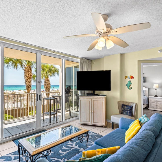 Unwind in your bright, coastal living room, where soft breezes drift through open balcony doors framing turquoise waters and swaying palms, inviting you to relax with the sea just steps away.