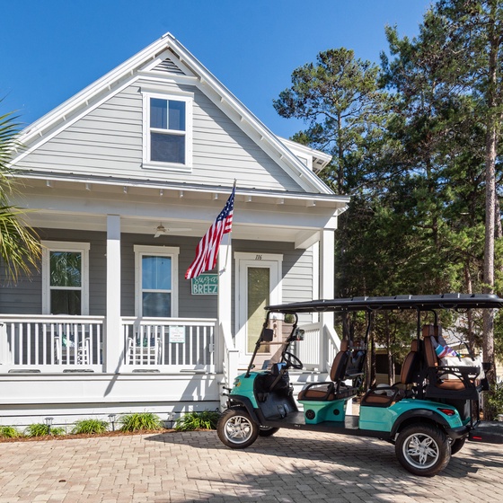Charming coastal cottage with welcoming front porch and convenient golf cart parking on brick pavers.