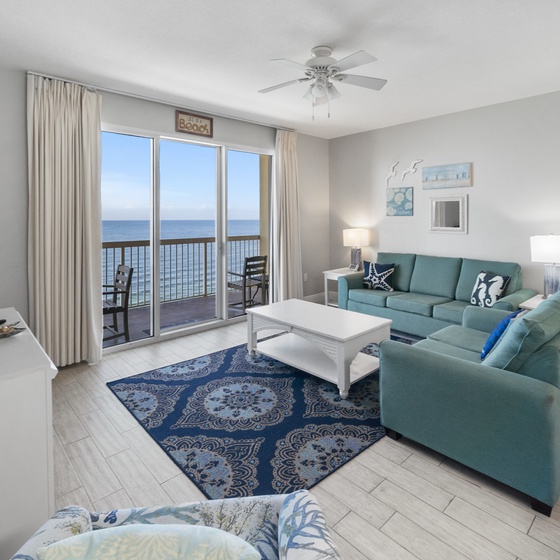 Your oceanfront living room invites you to unwind on plush teal sofas while enjoying panoramic sea views through floor-to-ceiling windows.