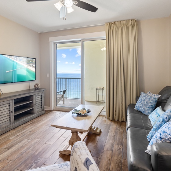 Relax in your coastal living room with ocean views through sliding doors, comfortable seating, and entertainment center.