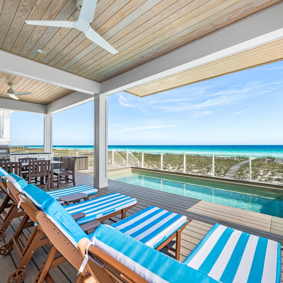 A covered deck features turquoise ocean views, a private pool, outdoor dining, and lounge chairs—ideal for beachside relaxation and entertaining.